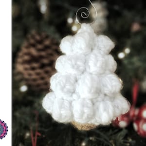 May include: White crocheted Christmas tree ornament with a wire hanger. The ornament is made with a puffy stitch and resembles a snow-covered tree.