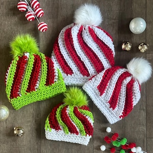 May include: Four handmade crochet hats in red, white, and green, with fluffy pom-poms. Two hats have red and white stripes, and two have red and green stripes. The hats are arranged on a wooden surface, with Christmas ornaments.