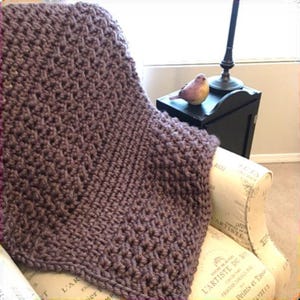 May include: A soft, purple knitted throw blanket with a textured pattern, draped over a chair with a floral print.