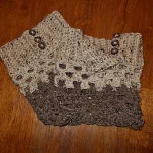 以下が含まれることがあります： 茶色とベージュのクロシェ編みブーツカフス。茶色のボタン付きです。