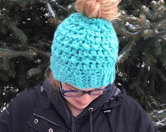 May include: A turquoise blue crocheted beanie with a hole in the top for a bun.