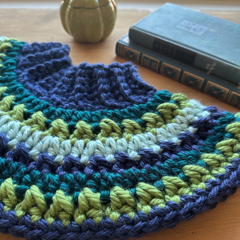 May include: A crocheted half-circle with a navy blue base and stripes of teal, light blue, and green yarn.
