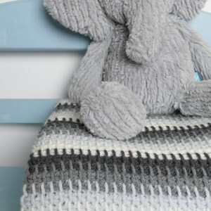 May include: A gray and white striped crocheted blanket with a gray plush elephant toy sitting on top of it.