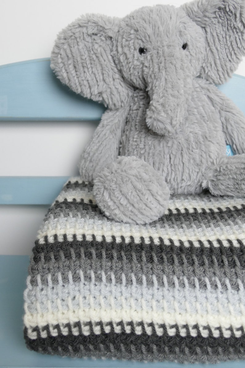 May include: A gray and white striped crocheted blanket with a gray plush elephant toy sitting on top of it.