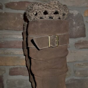 以下が含まれることがあります： 茶色のスエードブーツに茶色のクロシェの折り返しがあります。ブーツはバックル留めと折り返しデザインです。