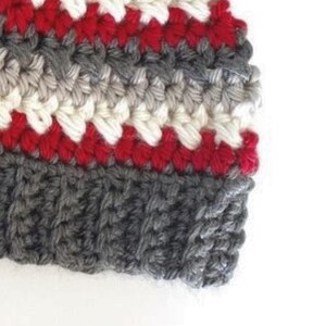 Peut inclure: Un chapeau crochet&eacute; avec des rayures de fil rouge, blanc et gris. Le chapeau a une bordure grise.