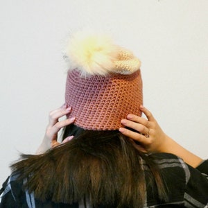May include: A pink and white crocheted beanie with a fluffy white pom pom.