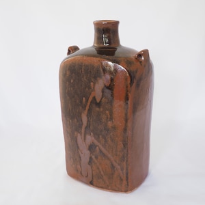May include: A brown ceramic vase with a square body and a narrow neck. The vase has two small handles on the sides and a brown glaze with a subtle floral design.