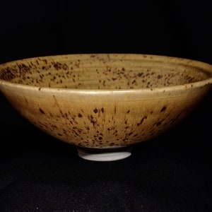 May include: A large, brown ceramic bowl with a speckled glaze. The bowl has a wide, shallow shape and a slightly flared rim.