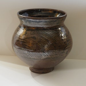 May include: A brown ceramic vase with a white glaze and a decorative pattern. The vase has a rounded body and a wide opening.