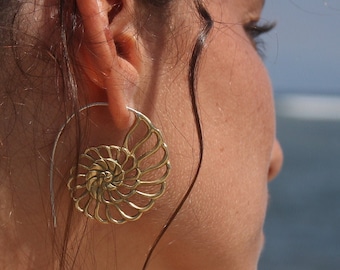 May include: A woman with long brown hair wearing a gold spiral shell earring.