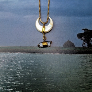 Puede incluir: Un collar de cadena dorada con un colgante de media luna de nácar blanco y un colgante de cristal transparente que cuelga de él.