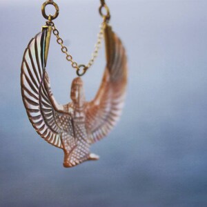 May include: A gold chain necklace with a detailed, carved, white and brown winged figure pendant.