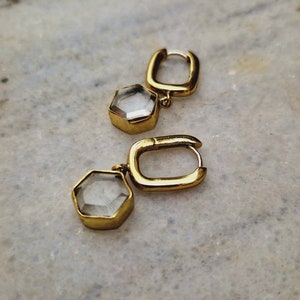 Puede incluir: Un par de pendientes de aro dorados con detalles de cristal hexagonal transparente.