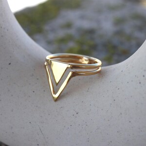 May include: A gold ring featuring a V-shaped design. The ring has a double band and a polished finish. The ring is a piece of jewellery, likely for fashion or adornment.