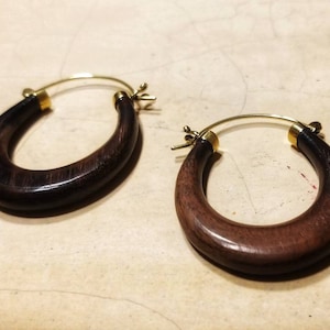Puede incluir: Un par de pendientes de aro de madera marrón oscuro con cierres de metal dorado.