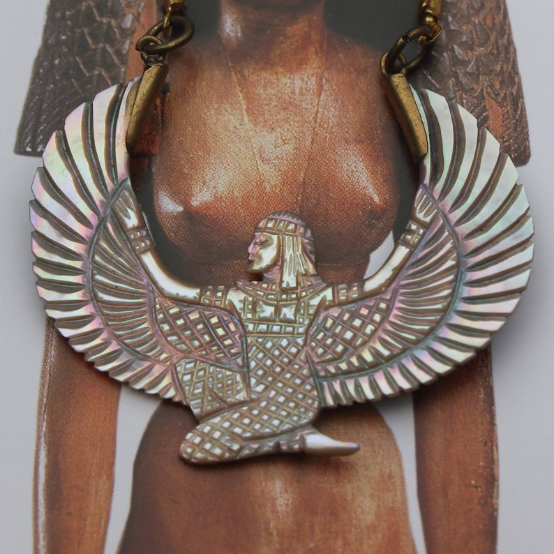 May include: A gold chain necklace with a large iridescent mother-of-pearl pendant featuring a winged goddess figure.