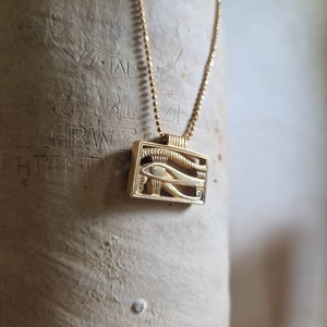 May include: A gold chain necklace with a pendant featuring the Eye of Horus, an ancient Egyptian symbol of protection and good health.