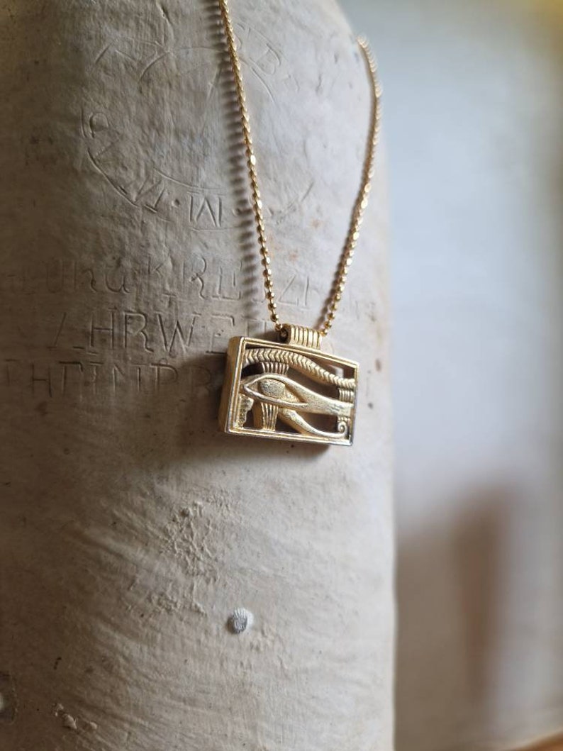 May include: A gold chain necklace with a pendant featuring the Eye of Horus, an ancient Egyptian symbol of protection and good health.