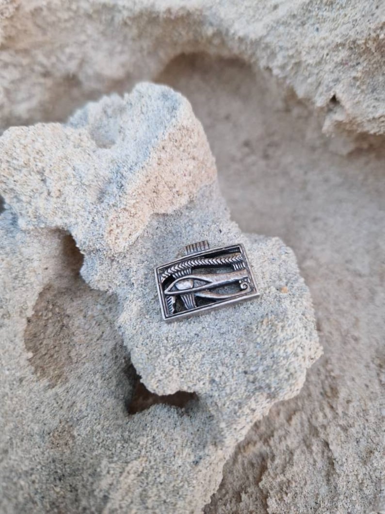 May include: Silver pendant featuring the Eye of Horus, an ancient Egyptian symbol of protection and good health. The pendant is rectangular and has a detailed design.
