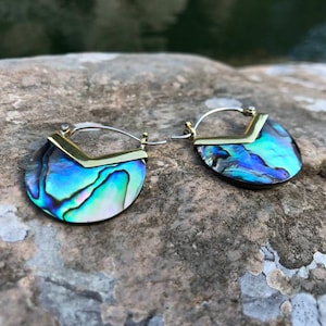 Puede incluir: Un par de pendientes de aro de oro y plata con un diseño de concha de abulón azul y verde. Los pendientes tienen forma de media luna.