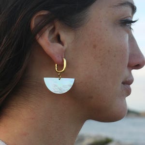 Puede incluir: Pendientes de aro dorados con un colgante de nácar blanco semicircular.