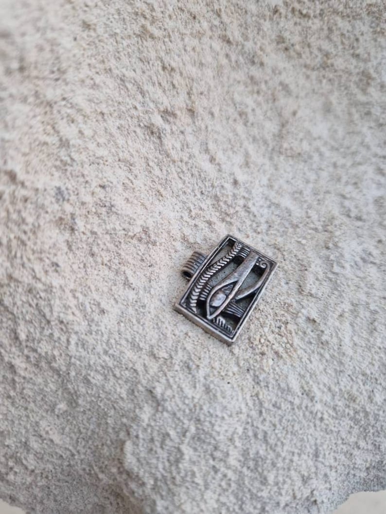 May include: Silver pendant featuring an intricate design of the Eye of Horus, a symbol of protection and good health in ancient Egyptian culture.