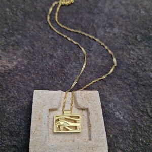 May include: A gold chain necklace with a pendant featuring the Eye of Horus, an ancient Egyptian symbol of protection and good health.