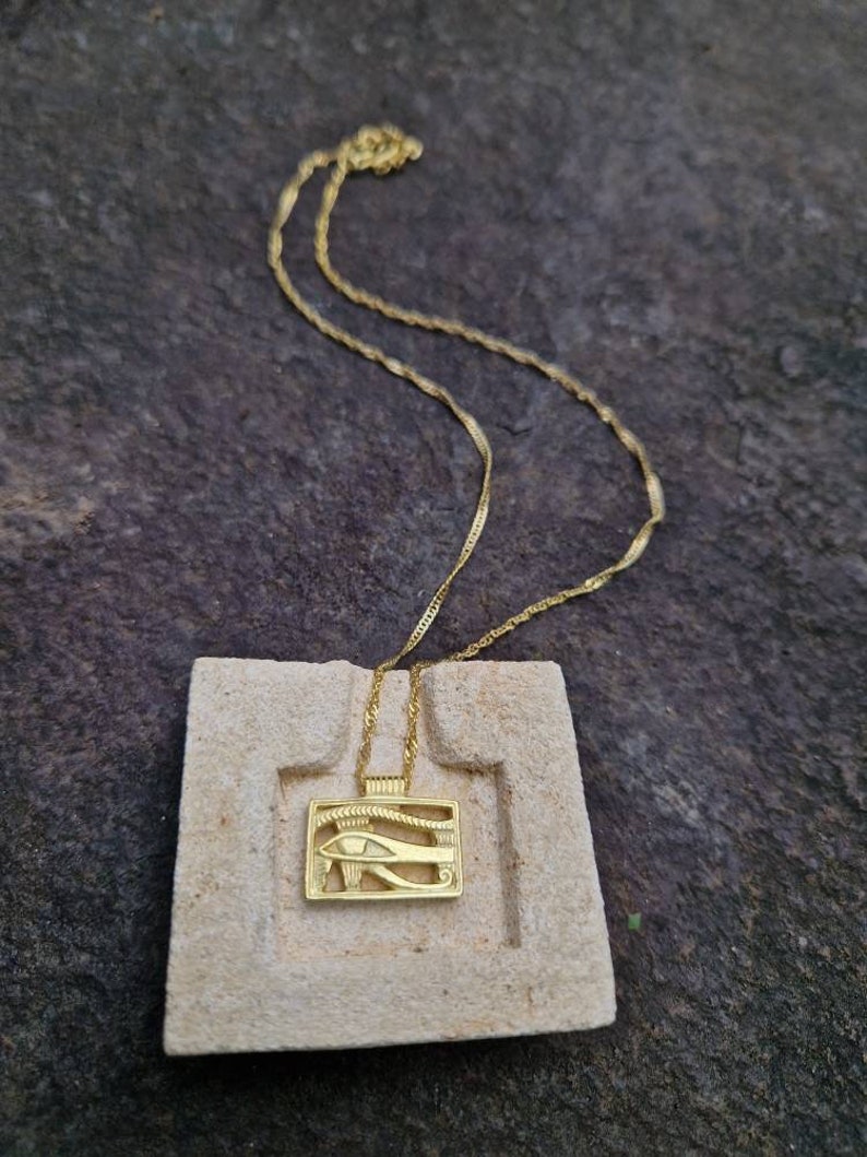 May include: A gold chain necklace with a pendant featuring the Eye of Horus, an ancient Egyptian symbol of protection and good health.