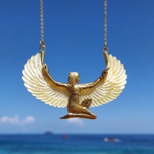 Puede incluir: Un collar de oro con un colgante que representa una figura alada con los brazos extendidos. El colgante está hecho de oro y tiene un acabado blanco nacarado. El collar está colgado sobre un fondo de cielo azul.