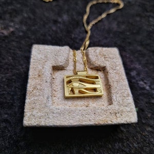 May include: A gold chain necklace with a pendant featuring the Eye of Horus, an ancient Egyptian symbol of protection and good health.