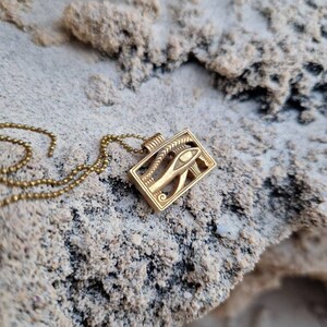 May include: A gold chain necklace with a pendant featuring the Eye of Horus, an ancient Egyptian symbol of protection and good health.