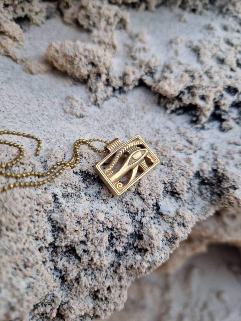 May include: A gold chain necklace with a pendant featuring the Eye of Horus, an ancient Egyptian symbol of protection and good health.