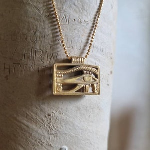 May include: A gold chain necklace with a gold pendant featuring the Eye of Horus, an ancient Egyptian symbol of protection.