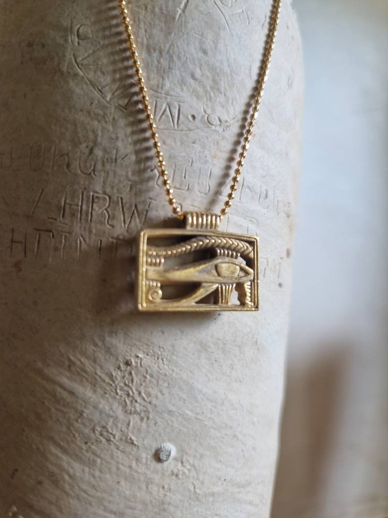 May include: A gold chain necklace with a gold pendant featuring the Eye of Horus, an ancient Egyptian symbol of protection.