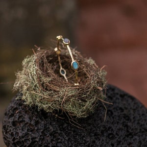 May include: A gold bangle bracelet with three oval-shaped blue gemstones set in the metal. The bracelet is sitting in a small bird's nest made of twigs and moss.