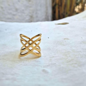 Puede incluir: Un anillo de color dorado con un diseño geométrico calado. El anillo está hecho de metal y tiene una forma cuadrada.