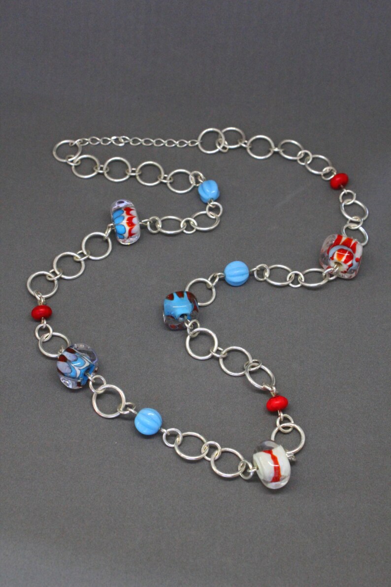 May include: A silver chain necklace with colorful glass beads. The beads are red, blue, and white with swirling patterns.