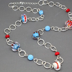 May include: A silver chain necklace with blue, red, and white glass beads. The beads have a variety of patterns and shapes.