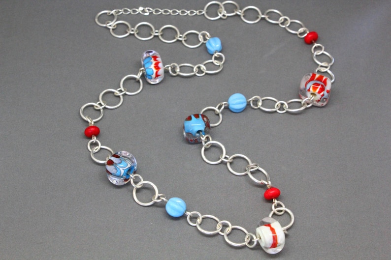 May include: A silver chain necklace with blue, red, and white glass beads. The beads have a variety of patterns and shapes.