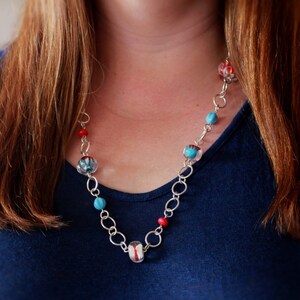 May include: A silver chain necklace with red, blue, and white glass beads. The beads have a floral pattern.