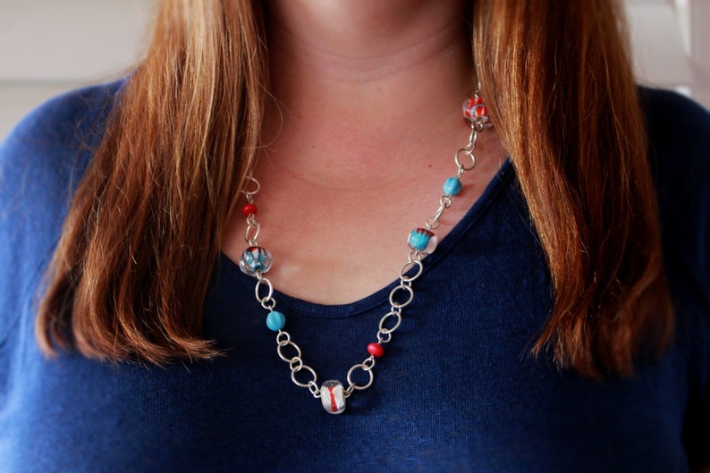 May include: A silver chain necklace with red, blue, and white glass beads. The beads have a floral pattern.