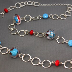 May include: A silver chain necklace with red, blue, and white glass beads. The beads have a swirling pattern.