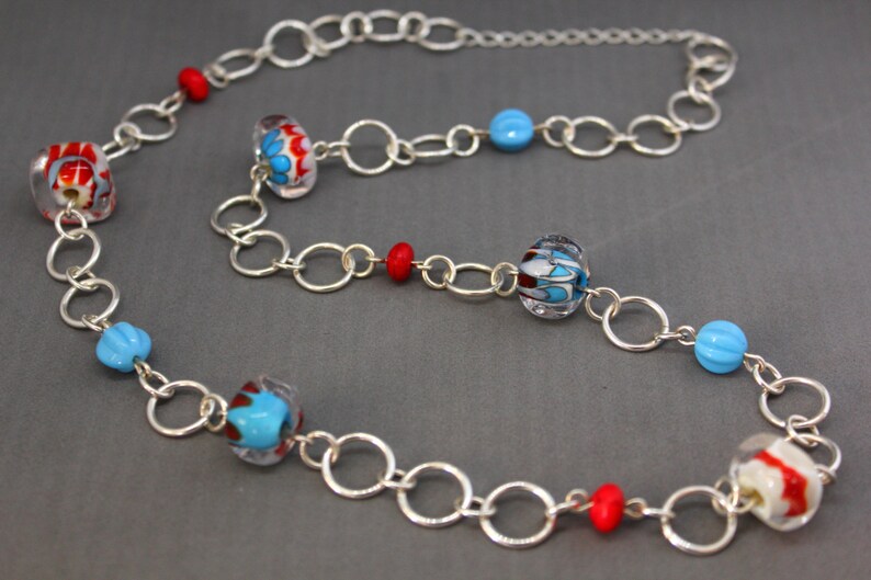 May include: A silver chain necklace with red, blue, and white glass beads. The beads have a swirling pattern.