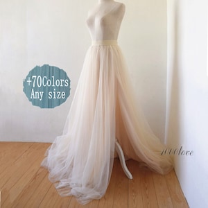 May include: A long, flowing tulle skirt in a light beige color. The skirt is gathered at the waist and falls to the floor. The skirt is displayed on a mannequin. The text '+70Colors Any size' is visible in the image.