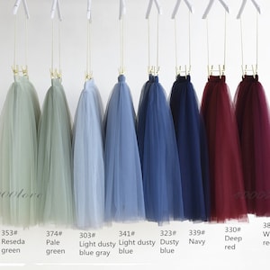 May include: Eight tulle skirts in different colors hanging on hangers. The colors are: reseda green, pale green, light dusty blue gray, light dusty blue, dusty blue, navy, deep red, and wine red.