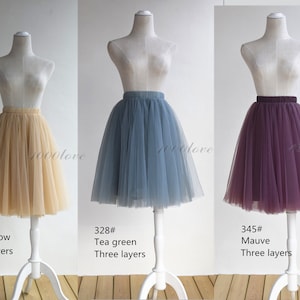 May include: Three tulle skirts in different colors: oats yellow, tea green, and mauve. Each skirt has three layers and is displayed on a white mannequin.