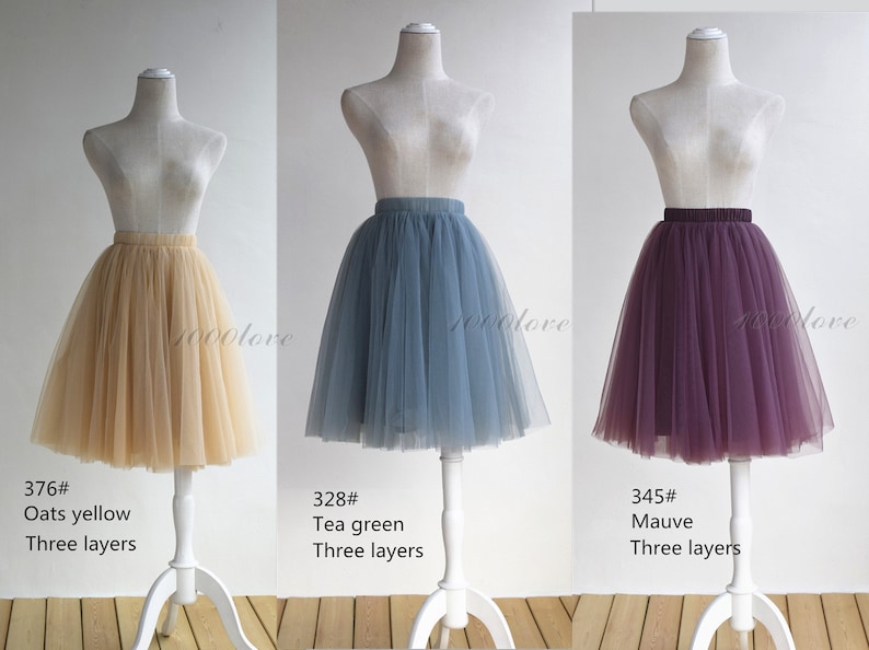 May include: Three tulle skirts in different colors: oats yellow, tea green, and mauve. Each skirt has three layers and is displayed on a white mannequin.