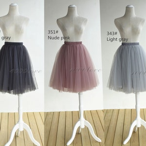 May include: Three tulle skirts in different colors: dark gray, nude pink, and light gray. The skirts are displayed on mannequins and are all the same style, with a full, gathered skirt and a waistband.