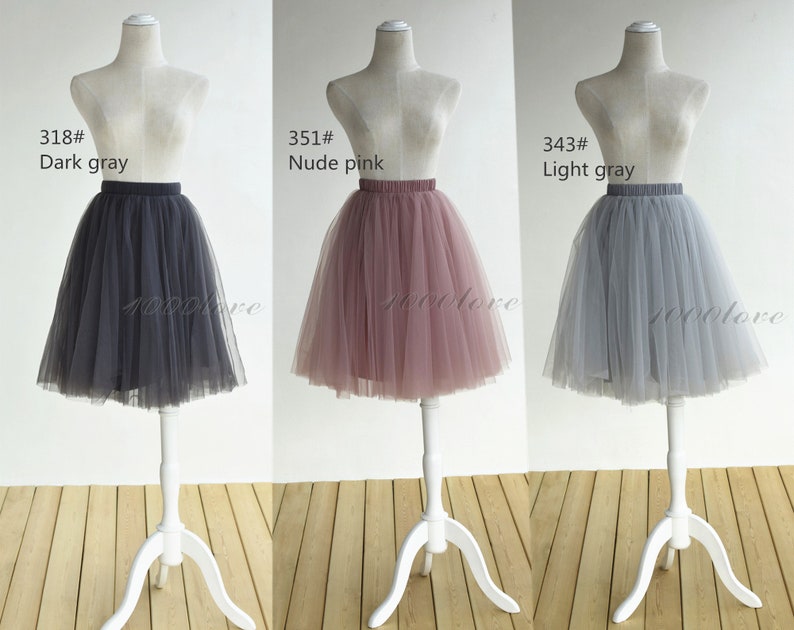 May include: Three tulle skirts in different colors: dark gray, nude pink, and light gray. The skirts are displayed on mannequins and are all the same style, with a full, gathered skirt and a waistband.